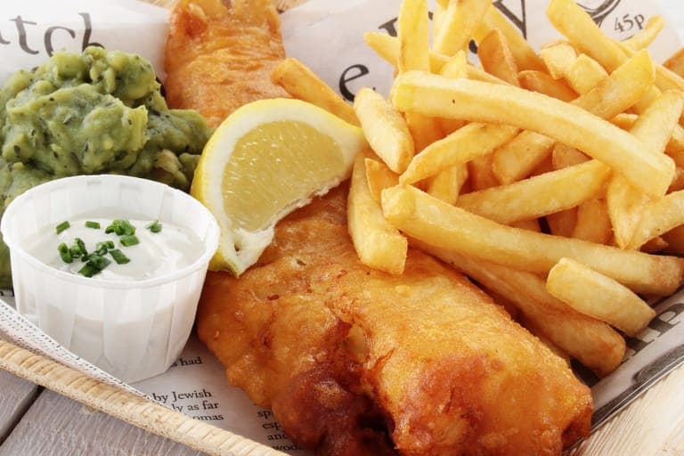 A basket of golden beer-battered fish and chips with mushy peas, lemon and tartare